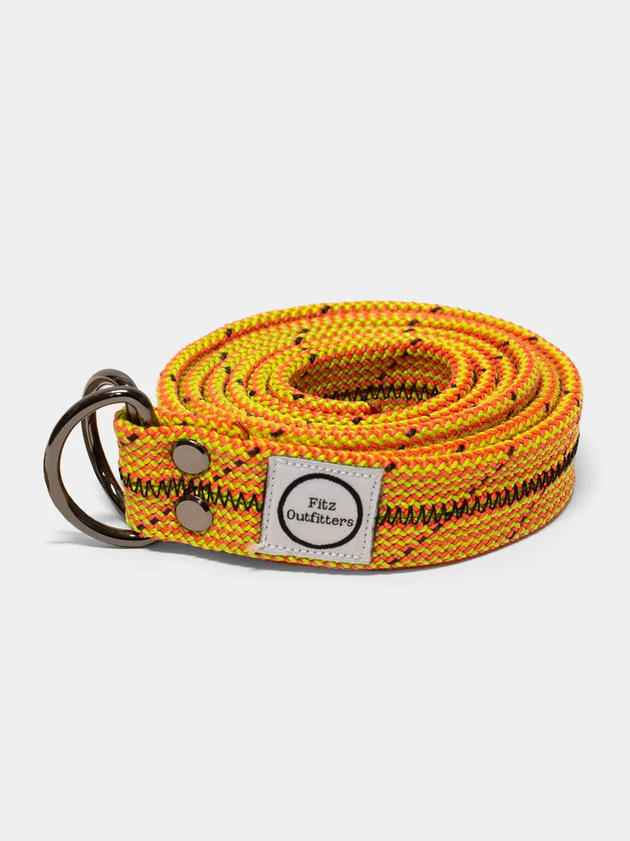 A multicolored climbing rope belt with a metal D-ring, displaying a pattern of orange and yellow with black ropes. A label with the brand 'Fitz Outfitters' is visible on the belt.