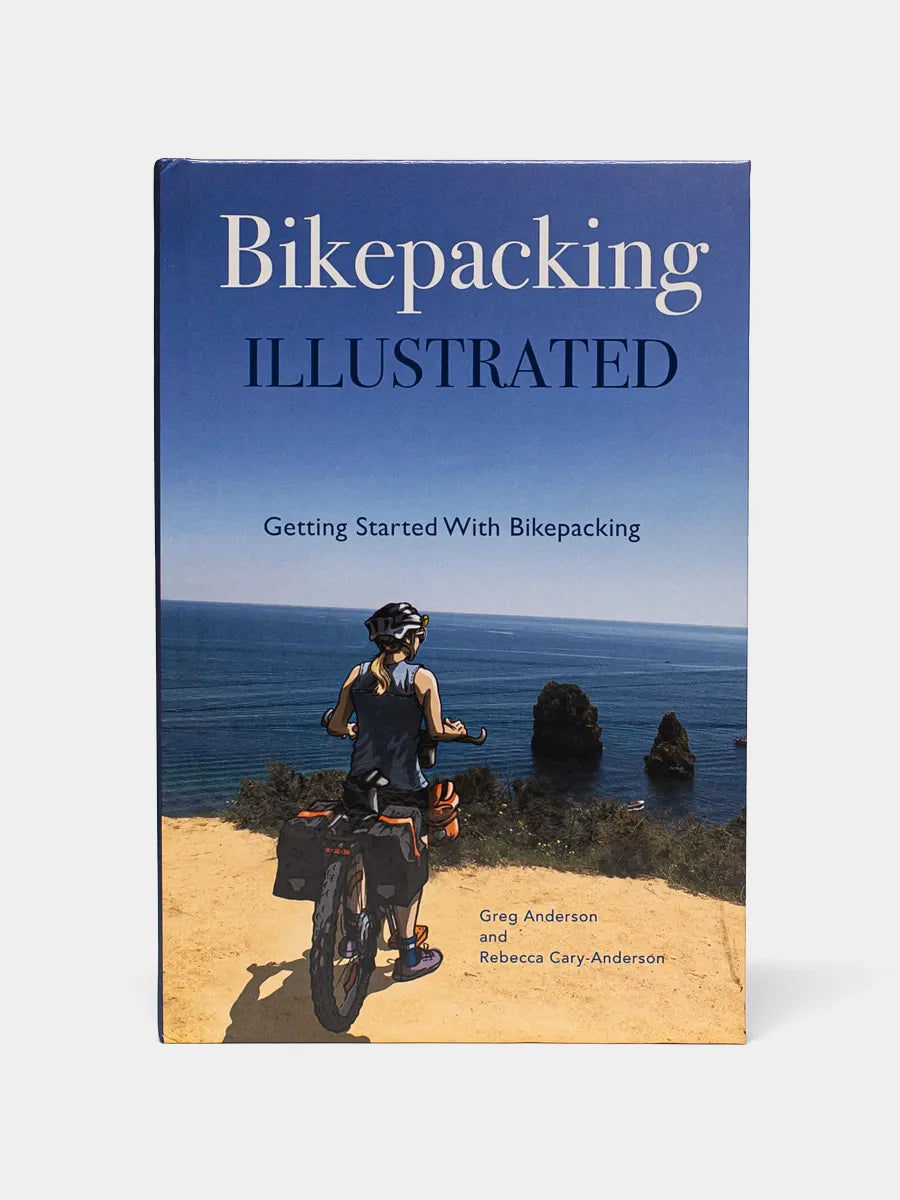 Front cover of Bikepacking Illustrated book shows a photo of a woman on a bike overlooking the ocean.