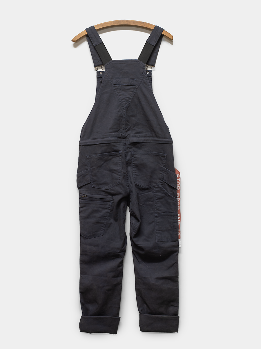 Black overalls with suspenders on a wooden hanger against a white background