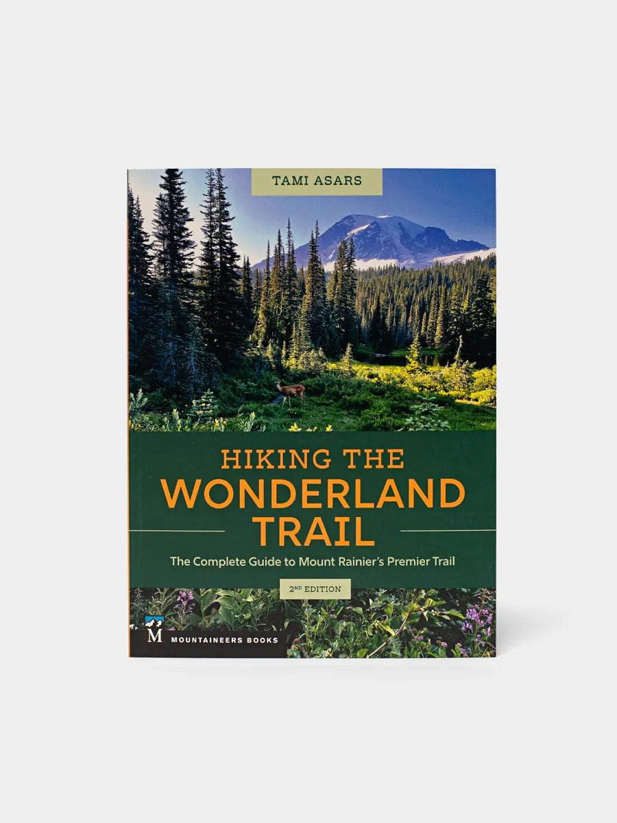 This image displays the cover of a book titled "Hiking the Wonderland Trail" by Tami Asars. The cover features a vibrant and inviting view of a lush forest leading up to a majestic mountain range, likely a scene along the所述 trail.