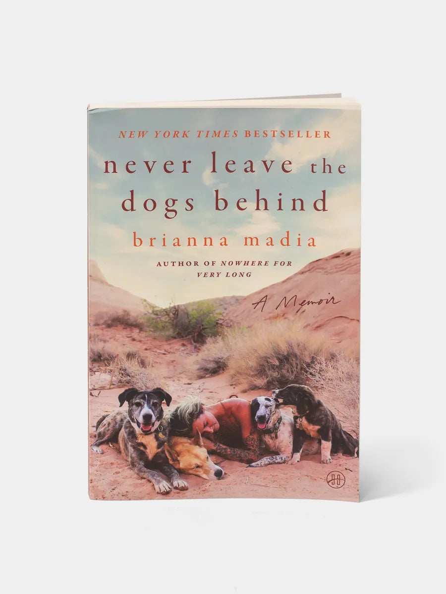 Front cover of Never Leave the Dogs Behind by Brianna Madia. A desert landscape sets the scene, with warm, dusty tones that echo the stark beauty of Utah’s backcountry. The title stands bold across the center, framed by an illustration of Brianna’s four dogs—Bucket, Dagwood, Birdie, and Banjo—her constant companions and co-stars of the story.