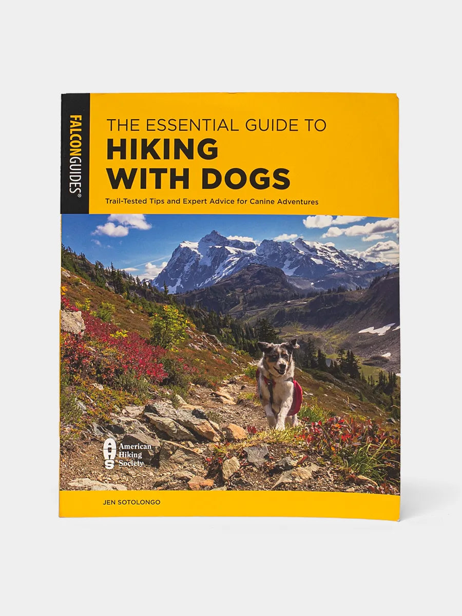 Front cover of “The Essential Guide to Hiking with Dogs” depicts a mountain landscape with an Australian Shepherd dog wearing a red pack on the trail.