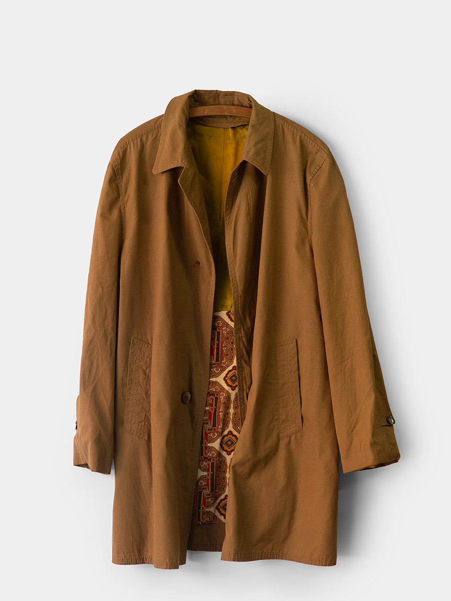 Vintage Mid Length Trench with a retro patterned lining on a white background hanging on a vintage wooden hanger.