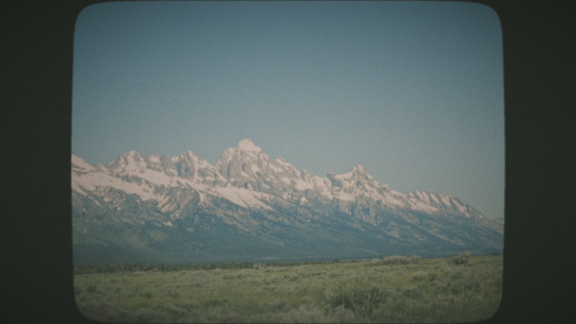 vintage retro video of a snow capped mountain range, with a lush valley in the foreground