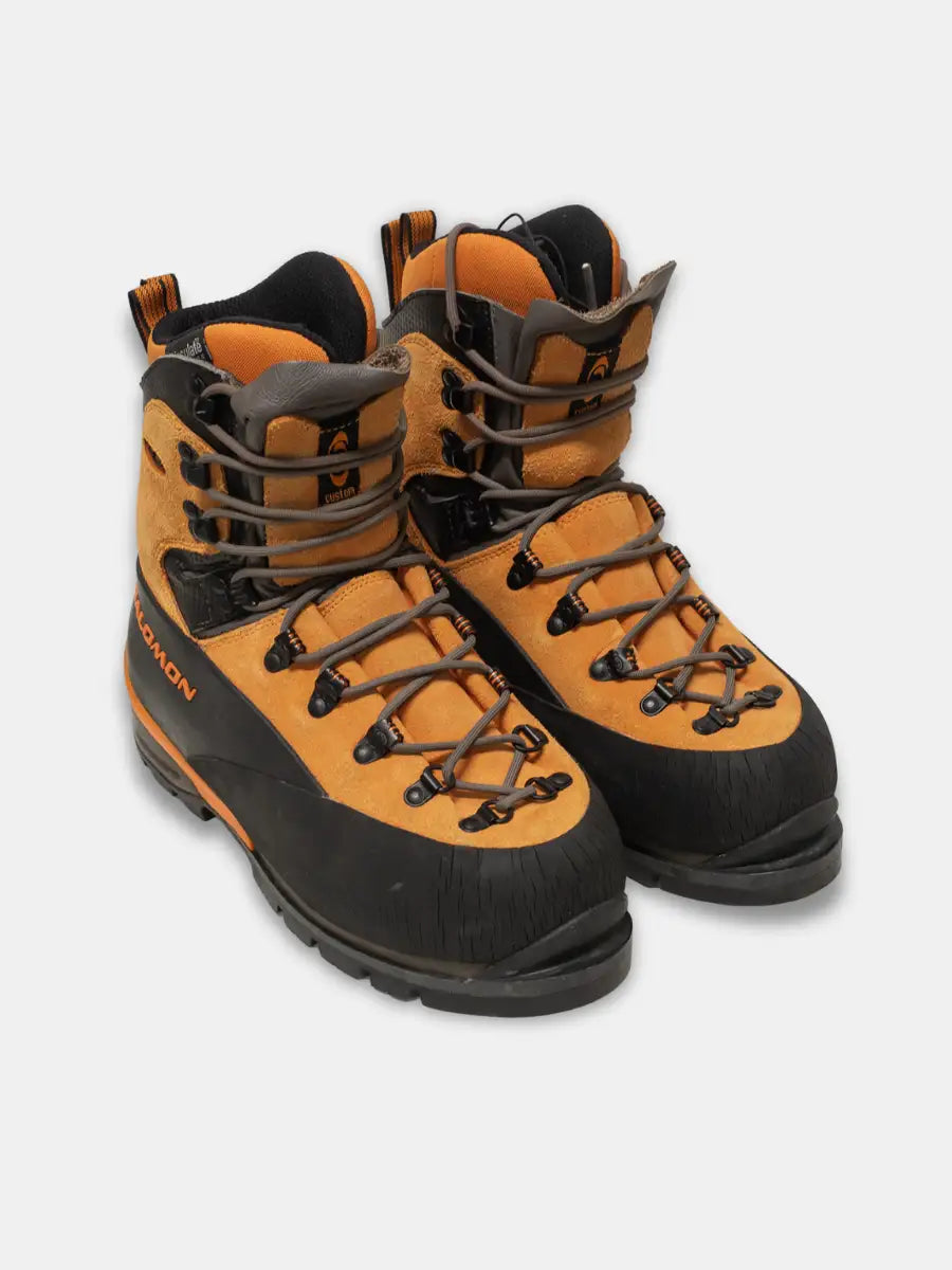 angled view, pair of Salomon Pro Thermic women’s mountaineering boots in orange and black with rubber rand and removable liner, photographed on white background.