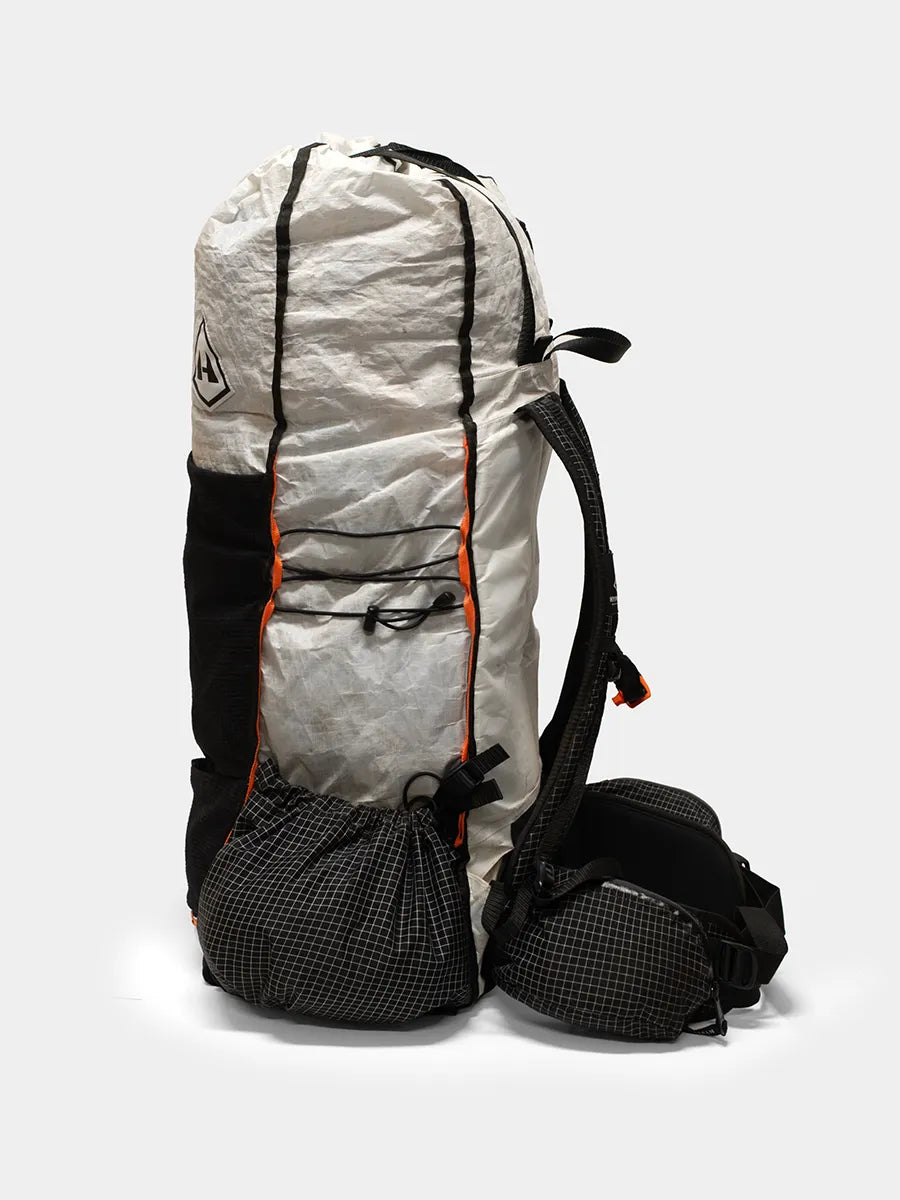 Side view of Hyperlite Mountain Gear Unbound 55 ultralight backpack in white and black with orange trim, showing front pocket and hip belt