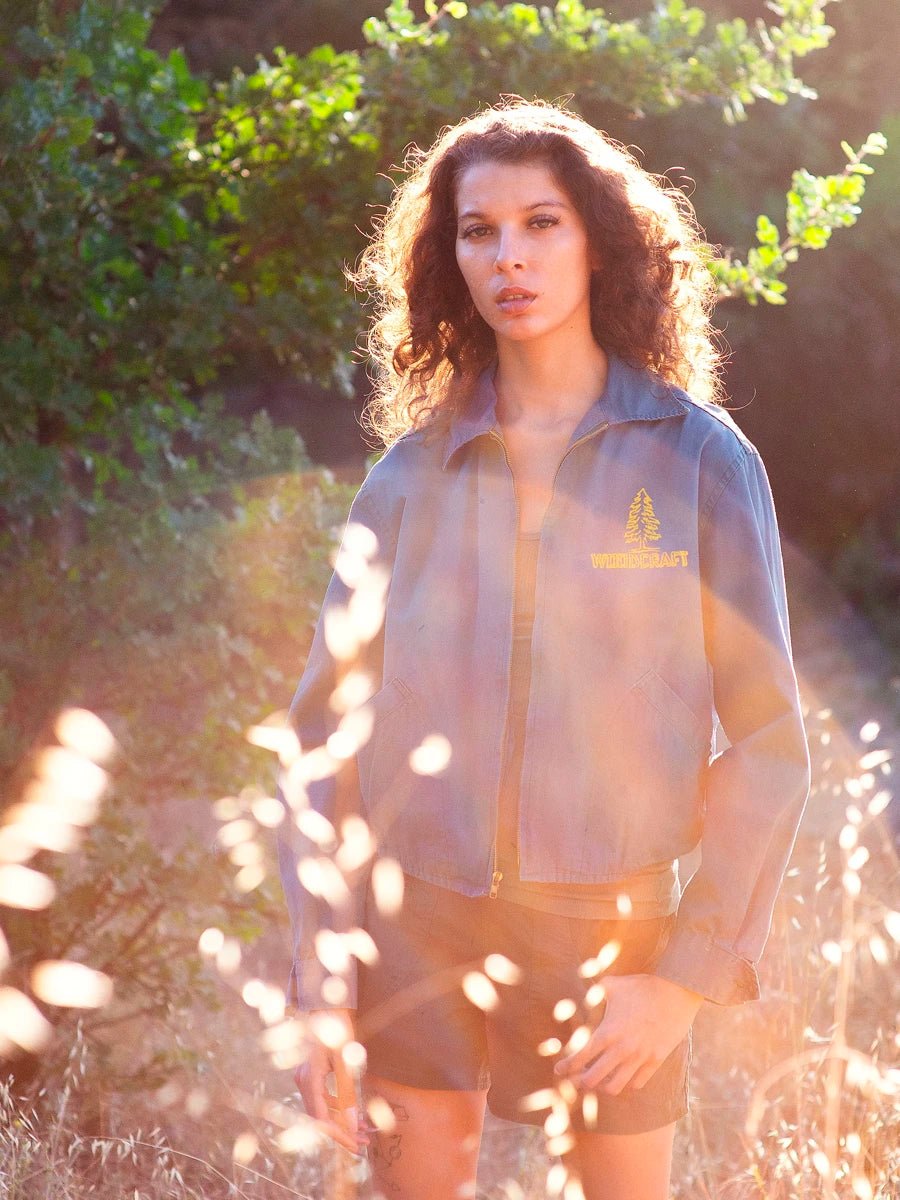 model wears Vintage Jacket and shorts in a sun drenched field. Image shows lens flare from sunlight